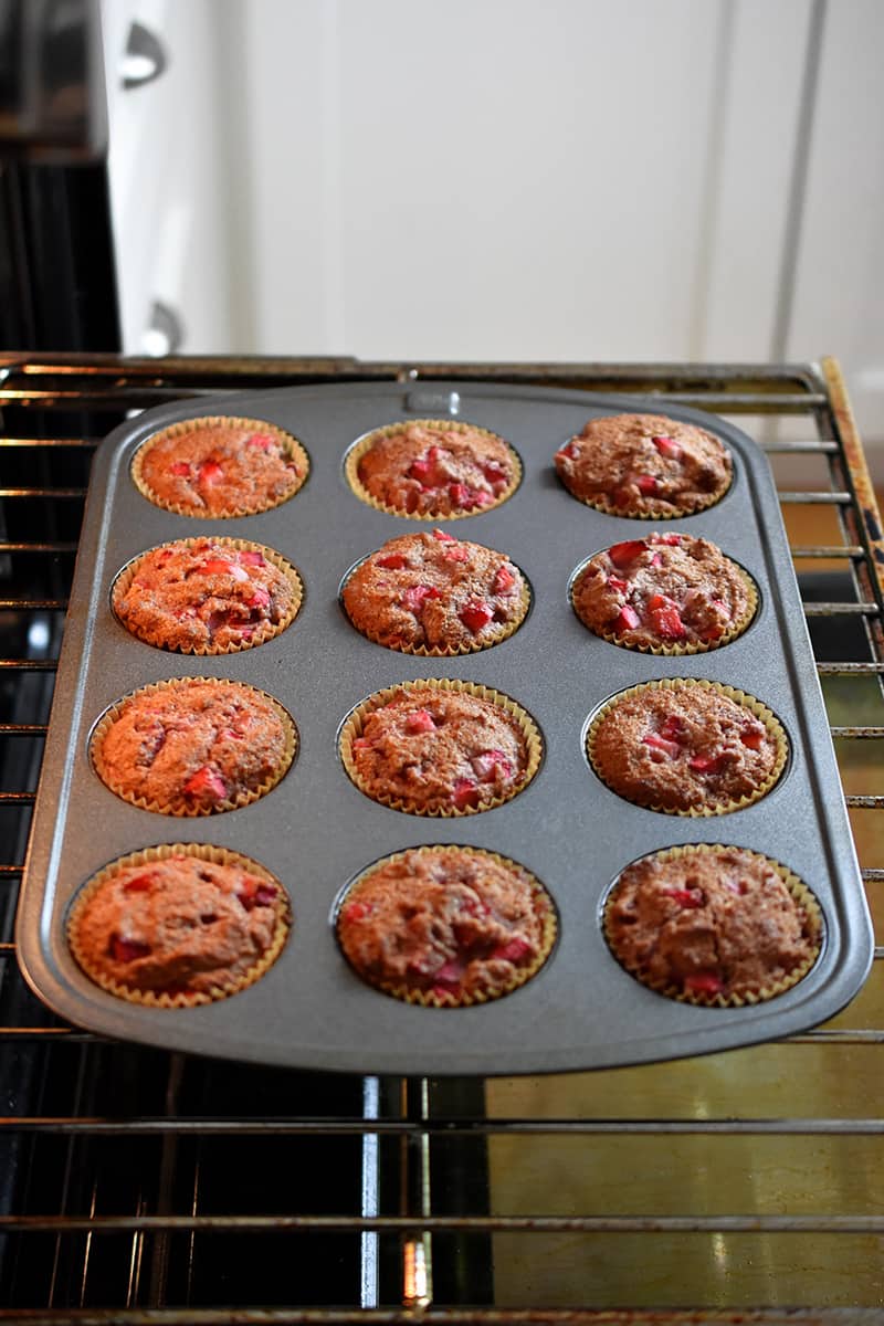 A muffin pan filled with golden brown strawberry muffins in an open oven.
