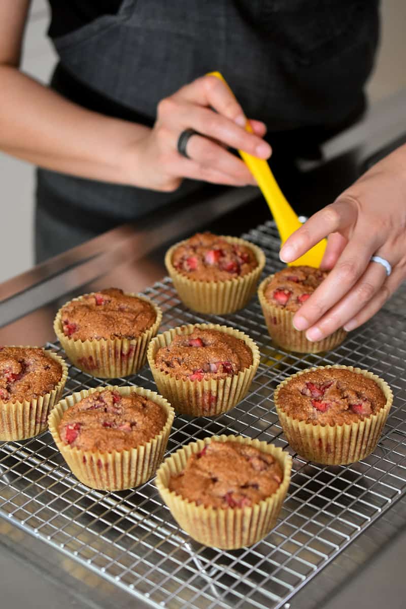 Two hands are transferring fresh baked gluten free paleo strawberry muffins onto a metal cooling rack.