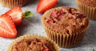Paleo strawberry muffins on a marble countertop surrounded by sliced strawberries.