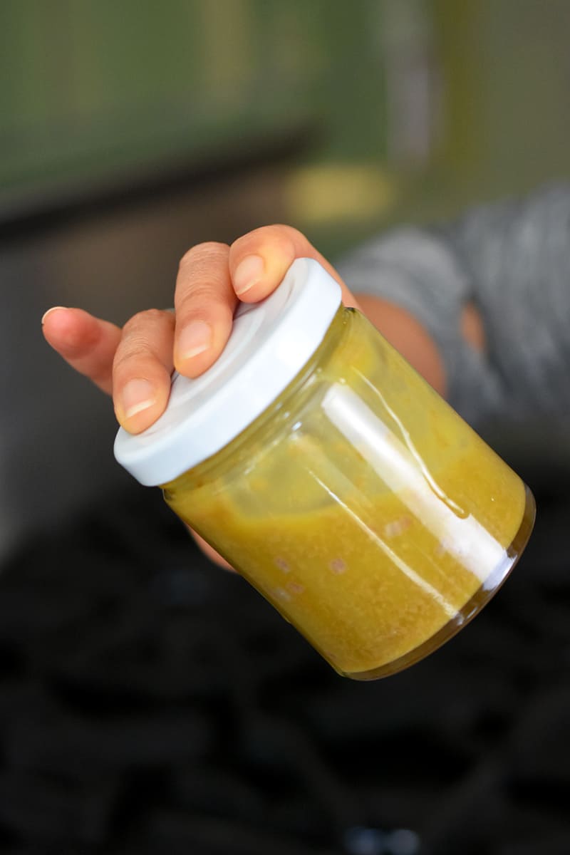 A hand is shaking a closed jar filled with garlic anchovy vinaigrette.