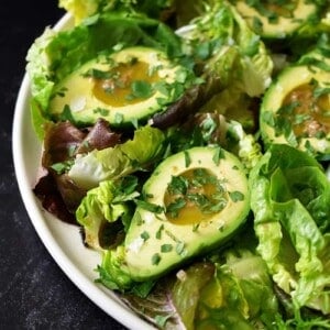 A side shot of avocado salad with garlic anchovy vinaigrette and topped with fresh herbs