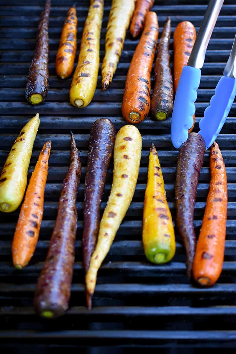 An overhead shot of rainbow colored carrots with char marks on a gas grill
