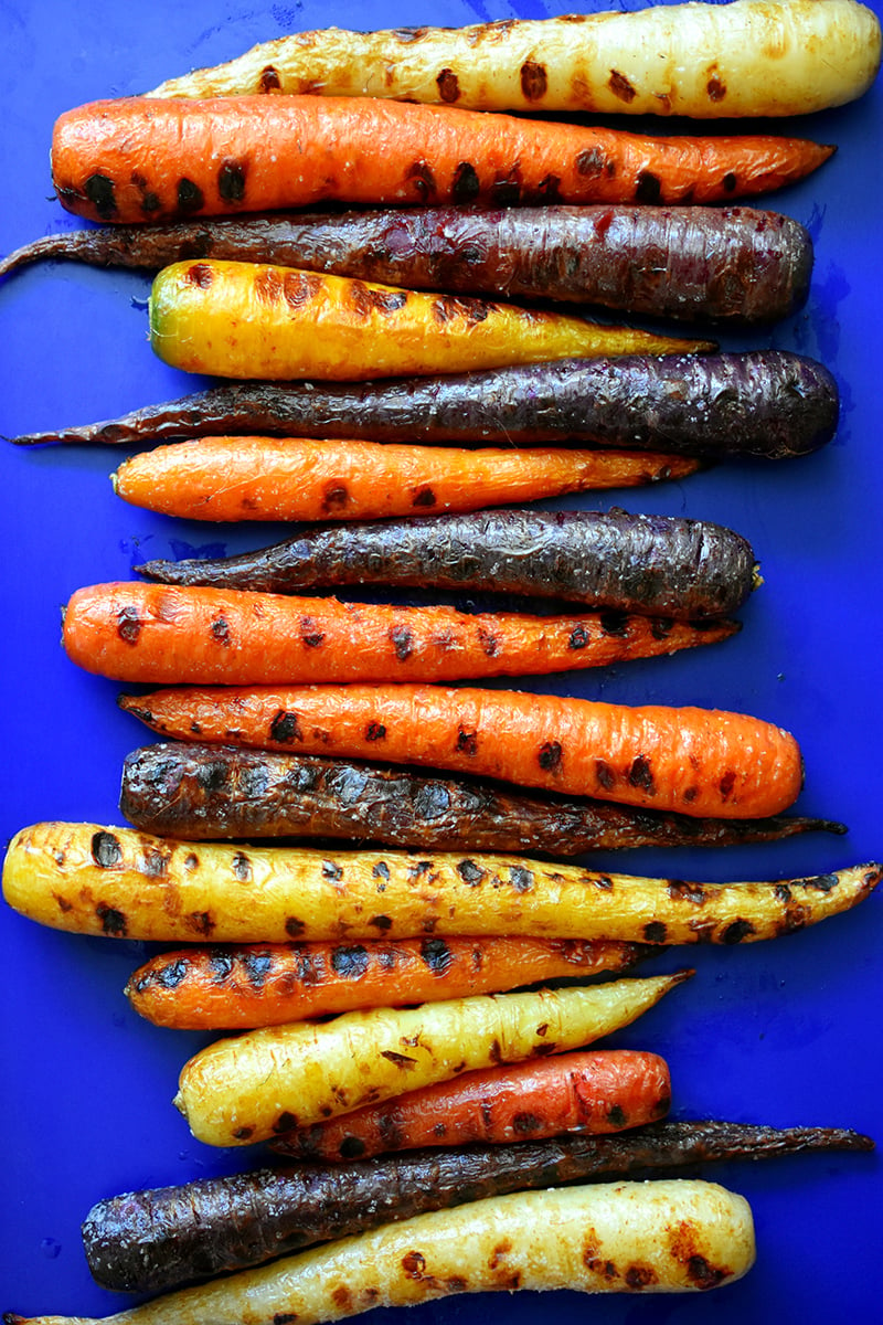 An overhead shot of a rimmed baking sheet topped with grilled rainbow colored carrots