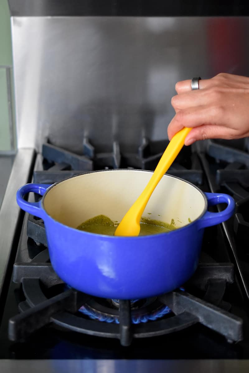A side shot of a yellow silicone spatula stirring reserved marinade in a blue saucepan on the stovetop
