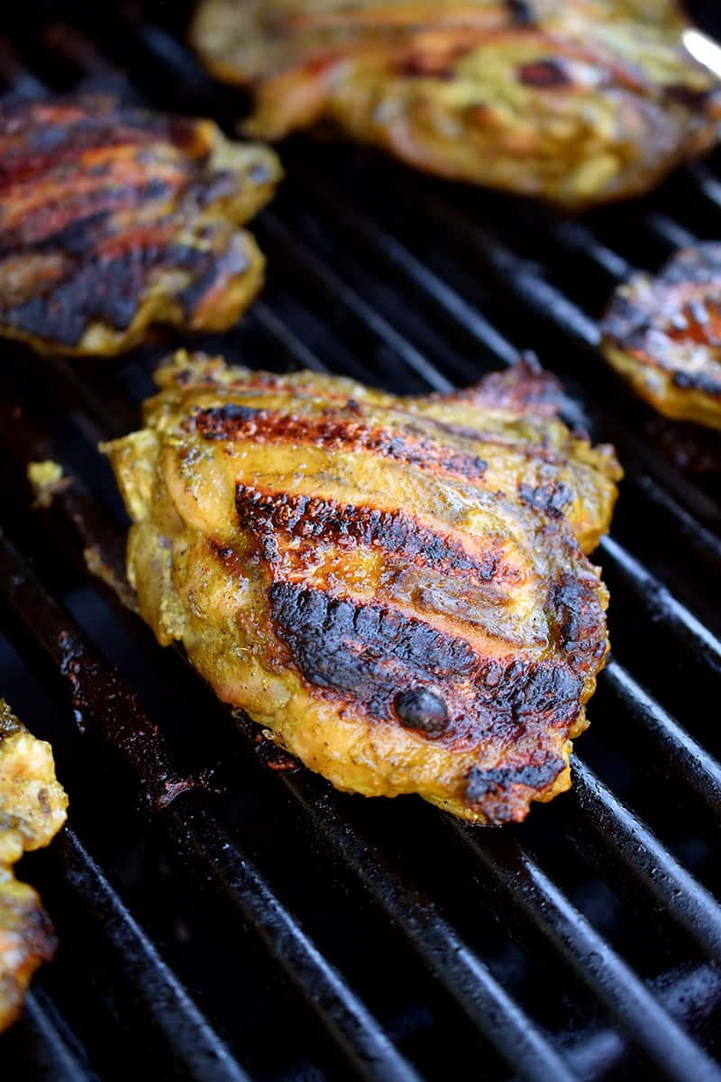 A closeup of chicken thighs on the grill with charred and crispy skin.
