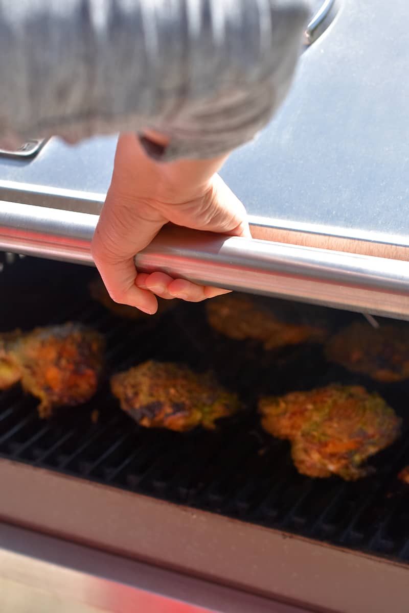 A hand is covering a grill filled with chicken thighs with the lid.