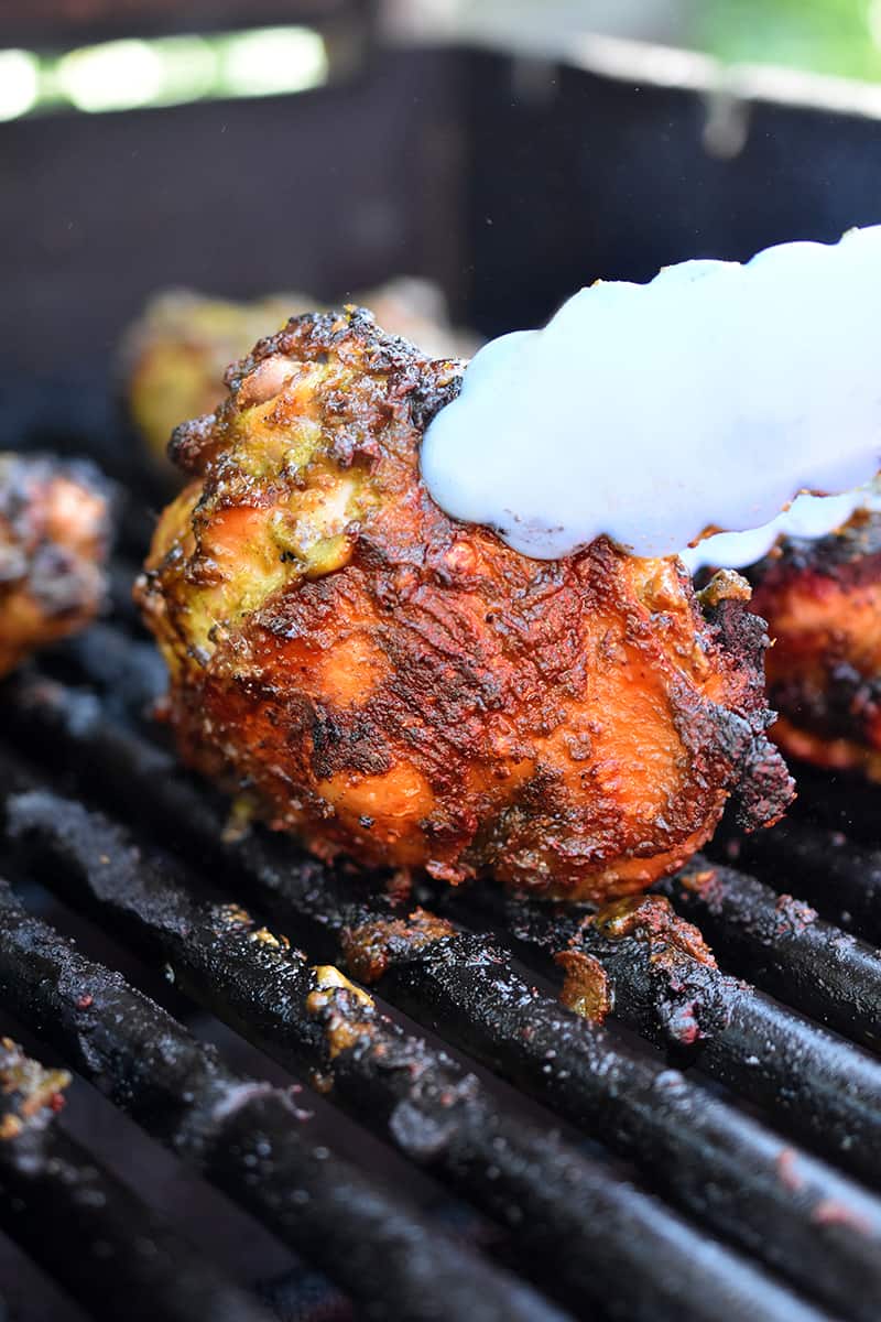 A closeup shot of a pair of tongs flipping a grilled chicken thigh.