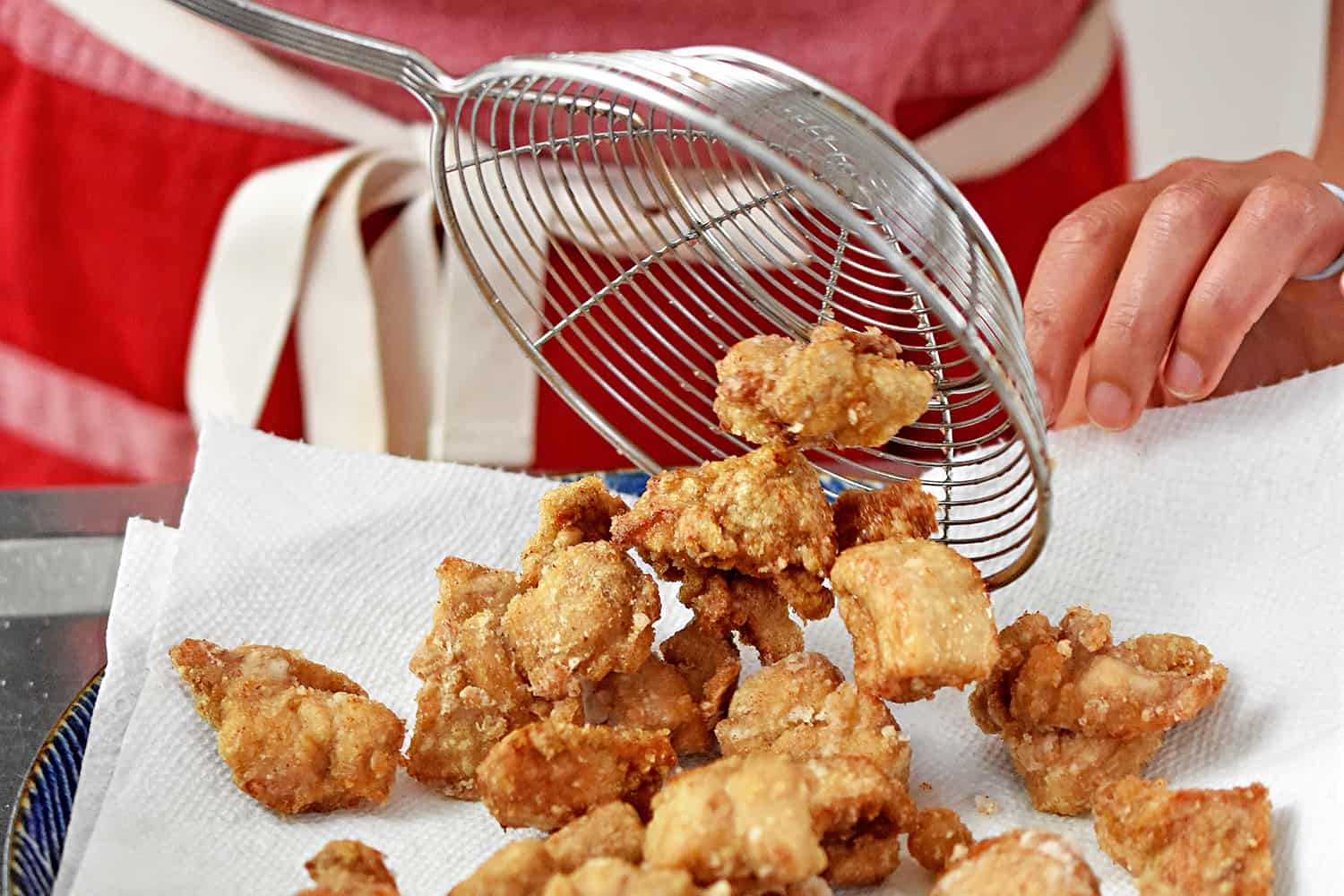 Transferring the deep fried Taiwanese popcorn chicken to a paper towel lined plate with a silver sieve.