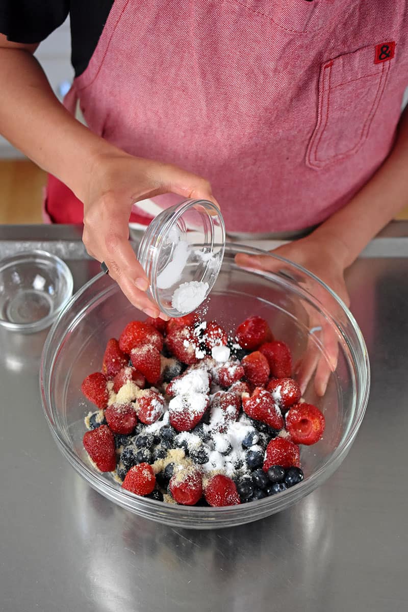 An overhead shot of someone adding tapioca flour to a bowl of mixed berries.