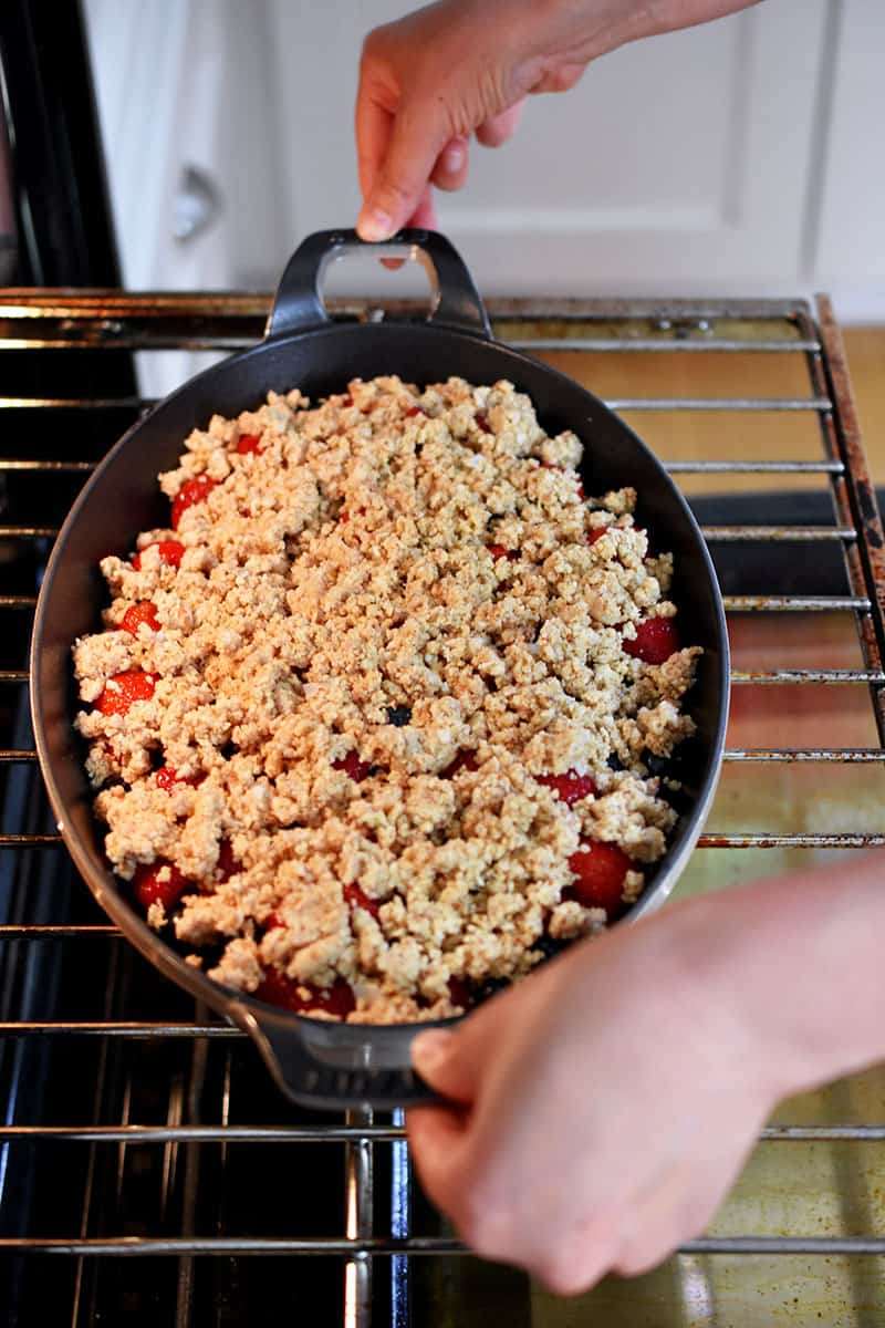 Two hands are placing the berry crisp into an open oven.