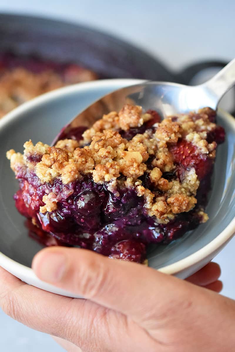 A close-up of someone scooping gluten-free berry crisp into a shallow bowl.