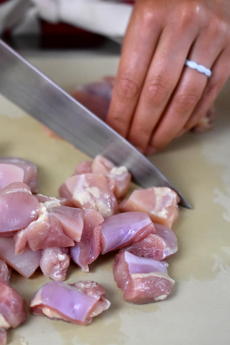 Someone is cutting up boneless, skinless chicken thighs into bite-sized pieces