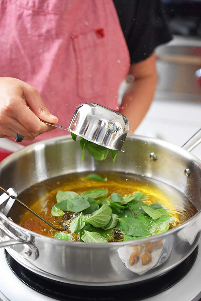 Adding Thai Basil to a pot filed with hot oil.