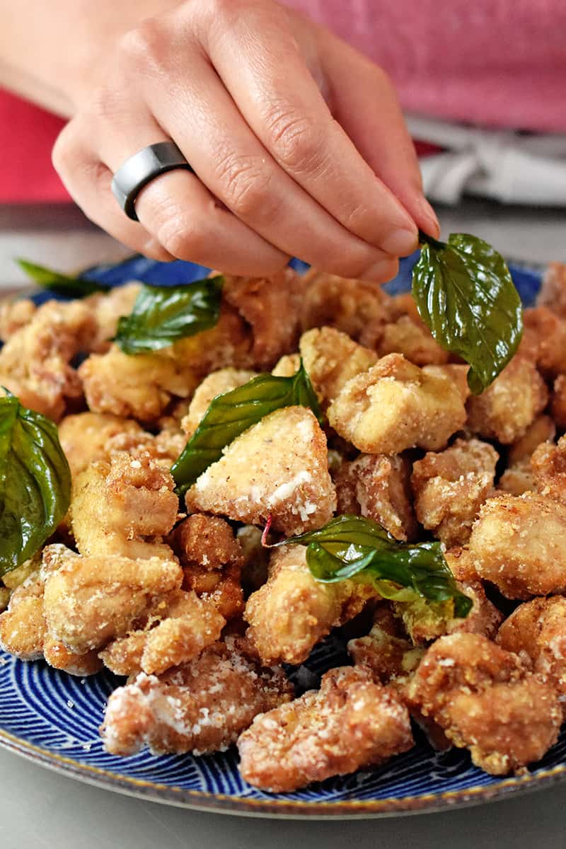 A hand is garnishing a platter of Taiwanese popcorn chicken with fried basil.