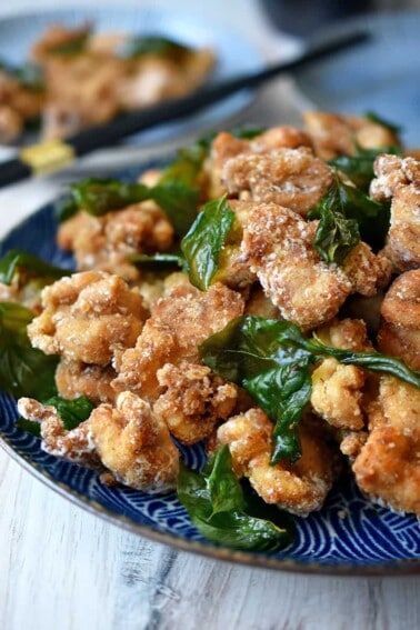 A side shot of a blue plate filled with gluten free and paleo Taiwanese popcorn chicken and fried basil