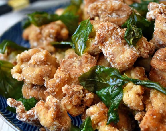A side shot of a blue plate filled with gluten free and paleo Taiwanese popcorn chicken and fried basil