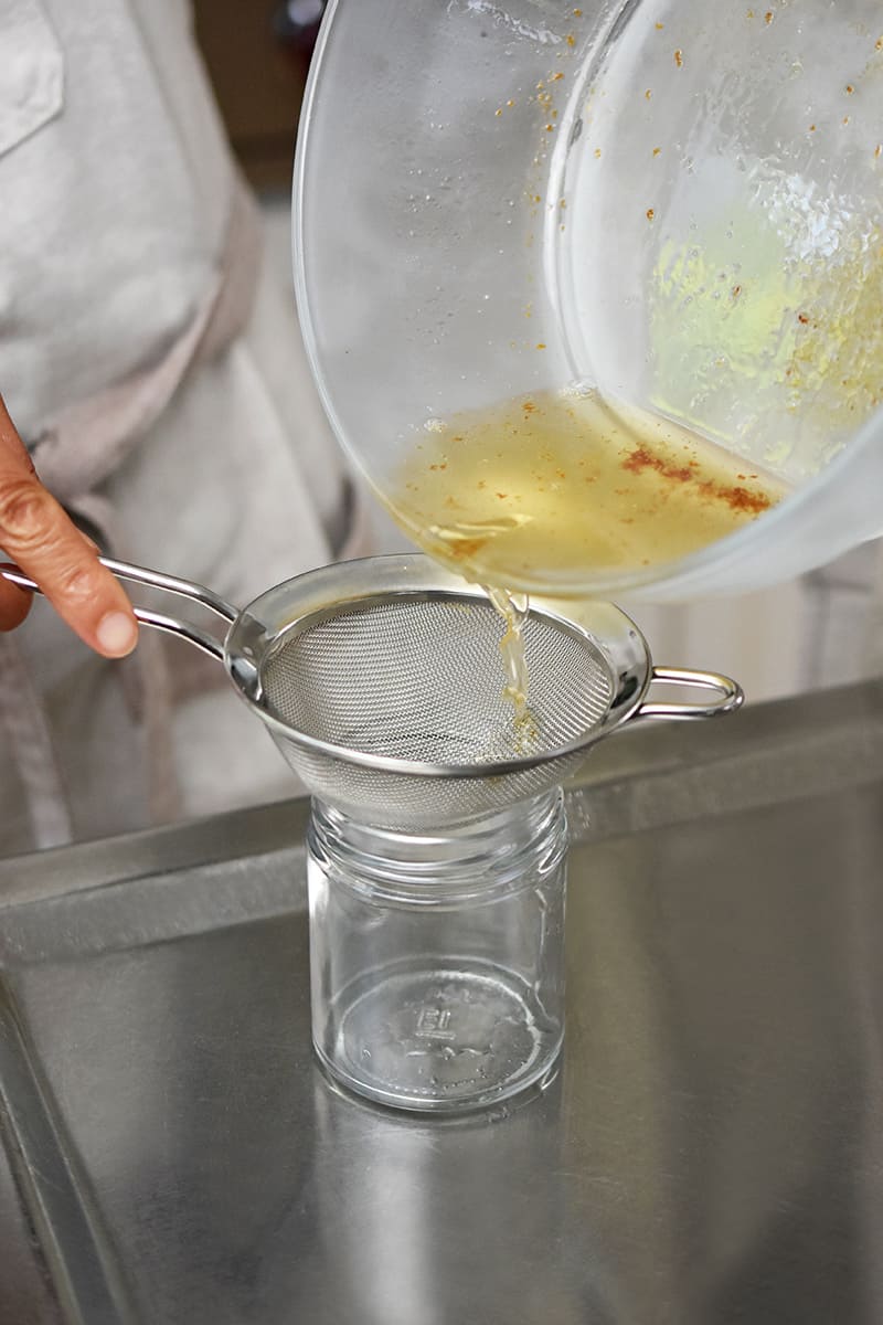 Pouring bacon drippings from a glass bowl to a jar with a fine mesh sieve