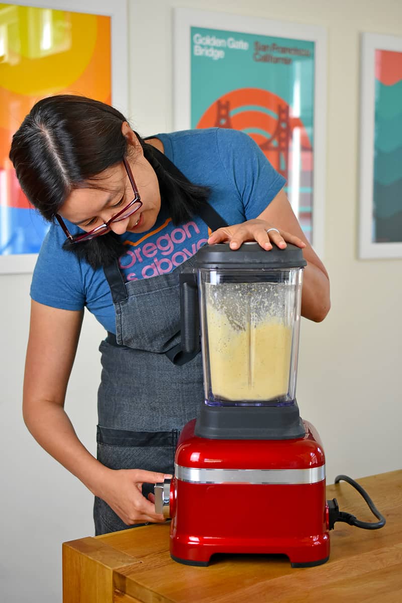 An Asian woman is blending mojo sauce in a red blender 