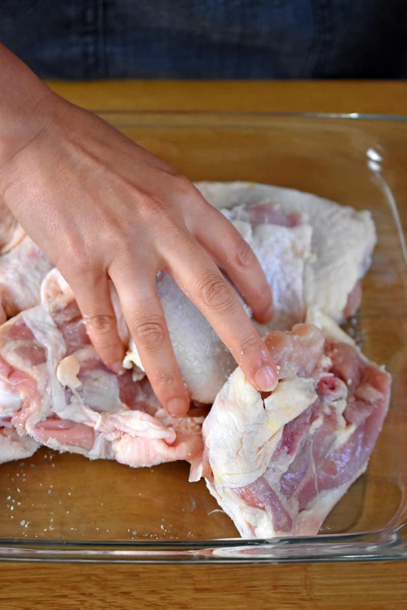 A hand is tossing chicken thighs in mojo marinade.