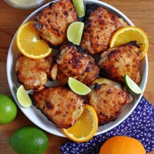 An overhead shot of a round platter filled with mojo chicken, mojo marinade, and oranges and limes.