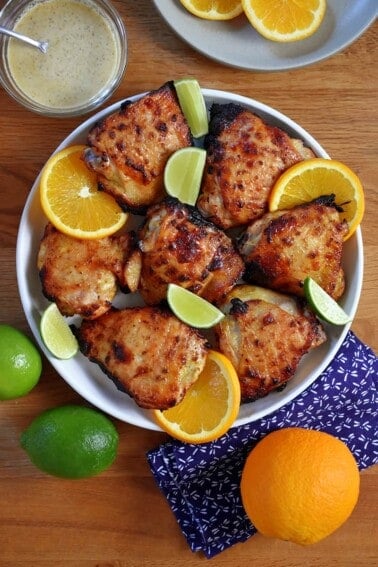 An overhead shot of a round platter filled with mojo chicken, mojo marinade, and oranges and limes.