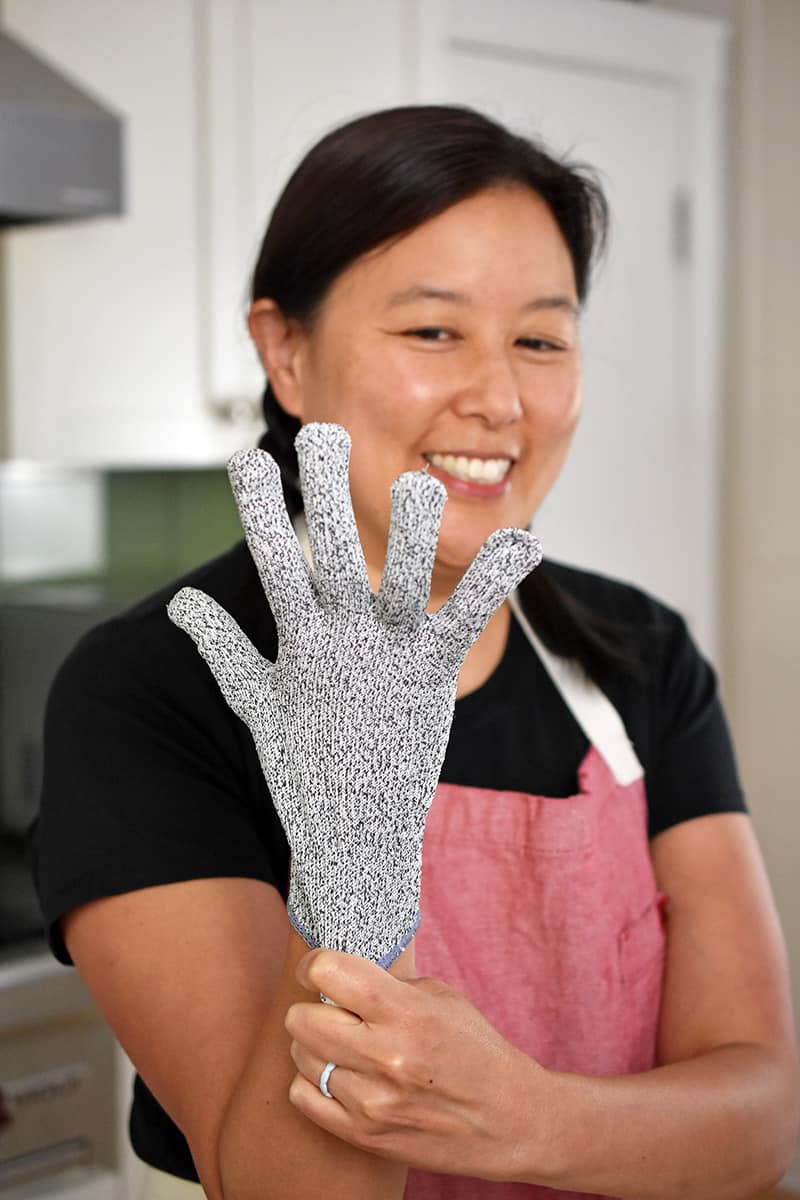 A smiling Asian woman is putting on cut resistant gloves