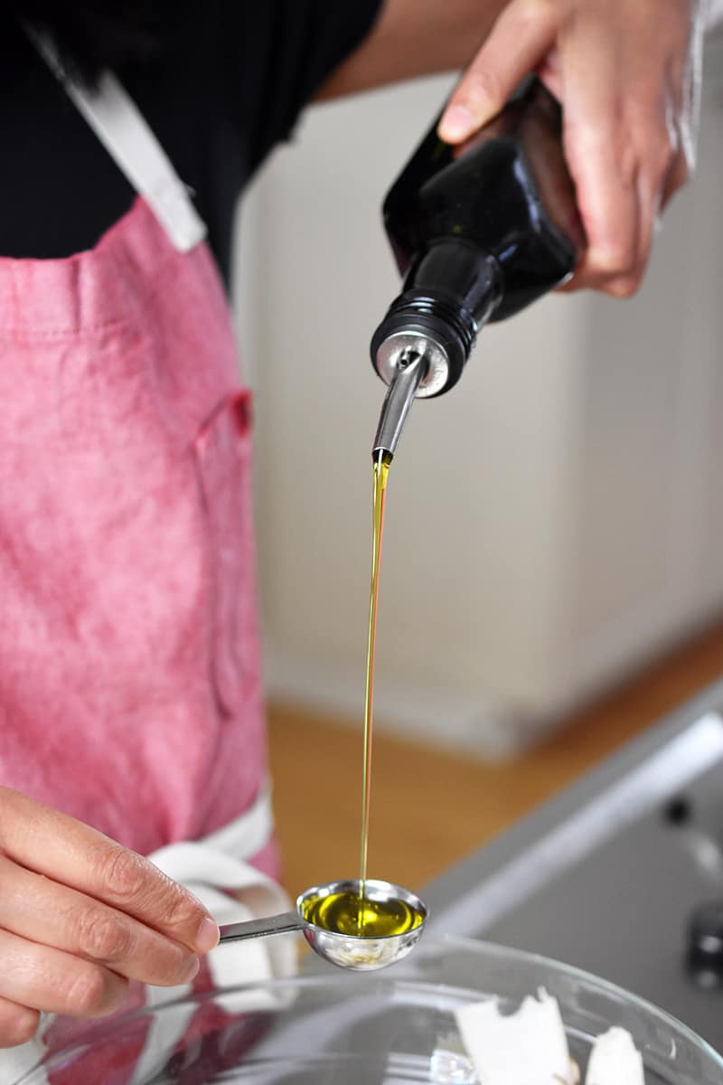 Pouring olive oil into a measuring spoon to add to king oyster mushroom salad