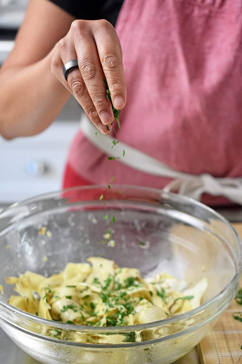 A person in a red apron is sprinkling fresh herbs on a bowl of mushroom salad