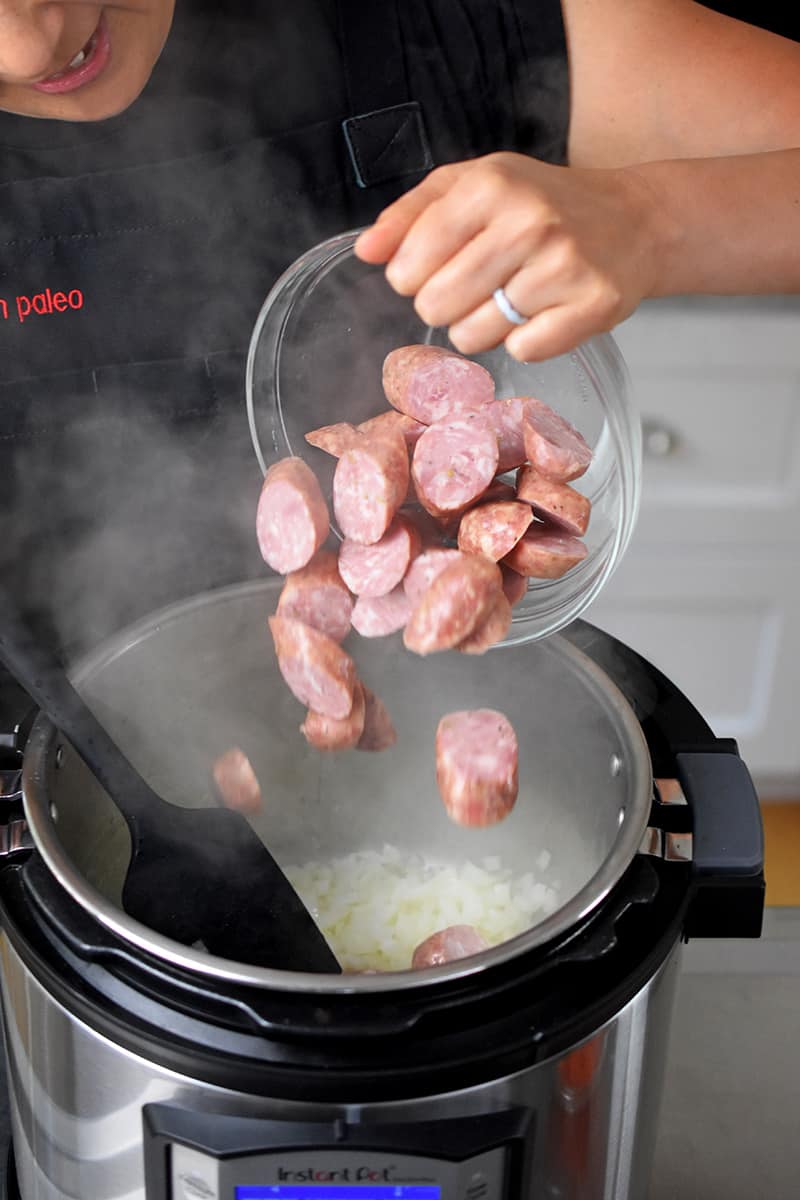 Someone adding sliced smoked sausage into an Instant Pot.
