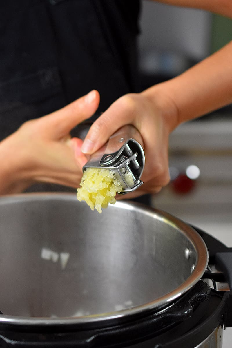 Someone adding minced garlic from a garlic press into an open Instant Pot