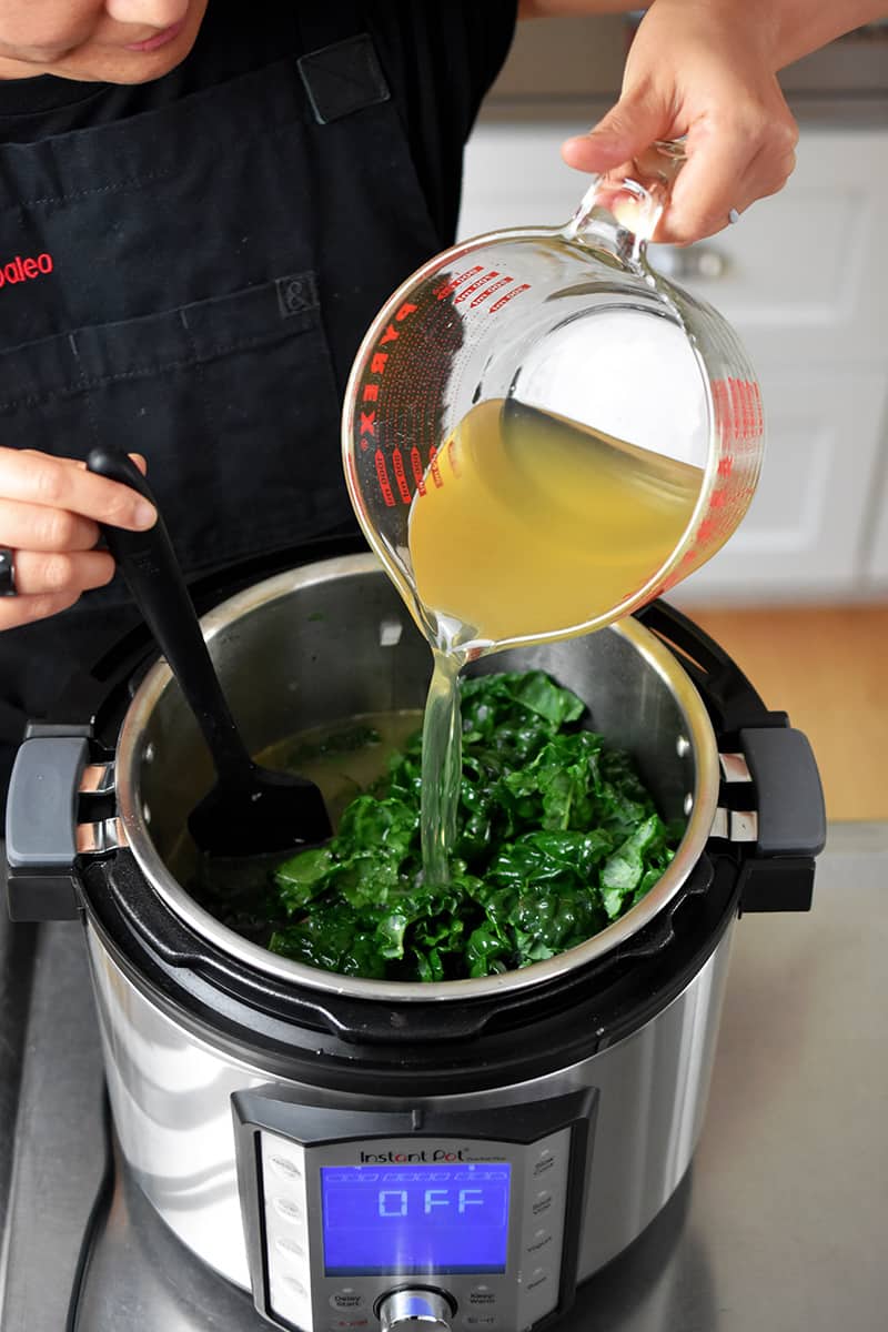 Pouring broth into an Instant Pot filled with kale, sausage, and the vegetables.