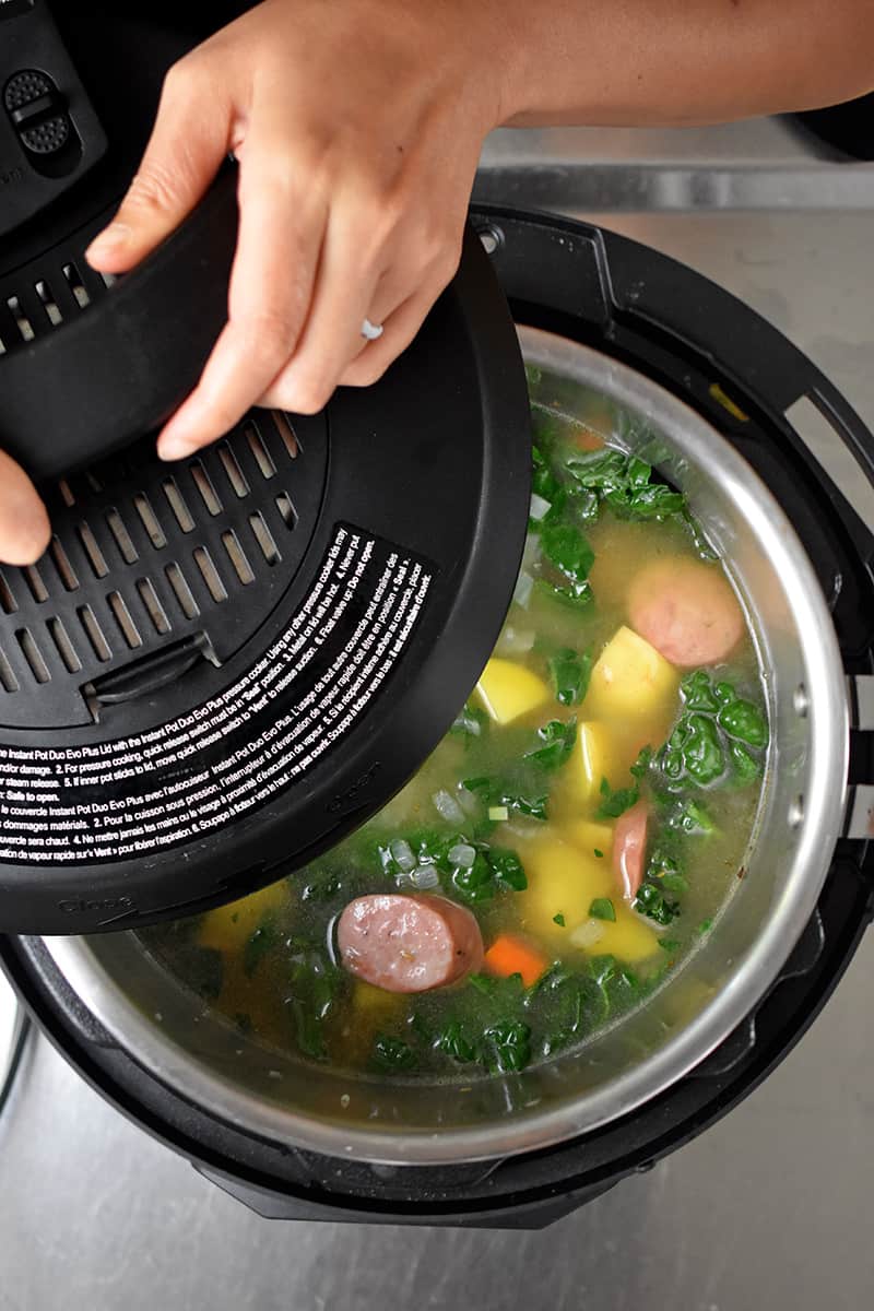 Someone placing a lid on an Instant Pot filled with kale sausage soup
