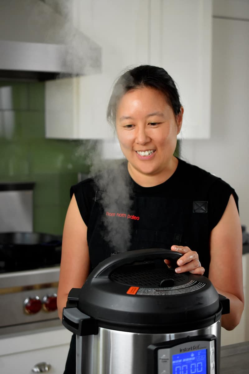 An Asian woman has manually released the pressure on an Instant Pot and steam is being released