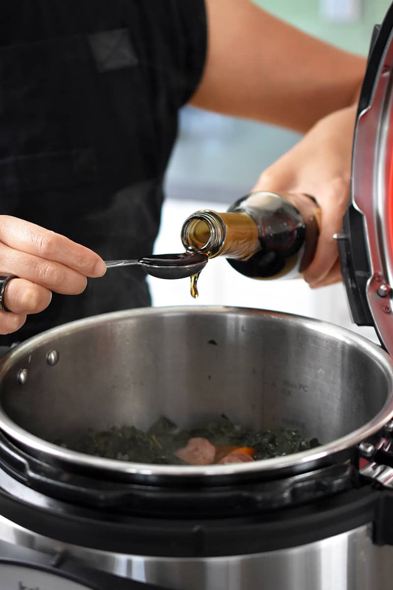 A person is measuring out a spoonful of sherry vinegar to add to Instant Pot sausage and kale soup