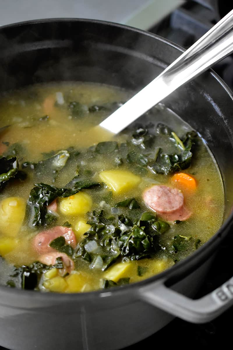 An side shot of a pot filled with steaming hot sausage and kale soup cooked on the stovetop