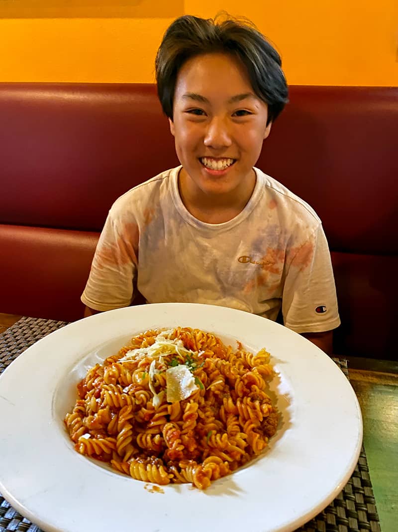 A smiling Asian teenager with a big bowl of gluten-free pasta from Pueo's Osteria on the Big Island