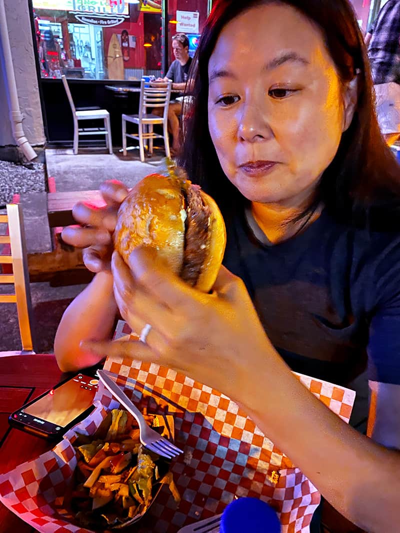 An Asian woman eating a gluten free burger from at Island Ono Loa Grill on the Big Island