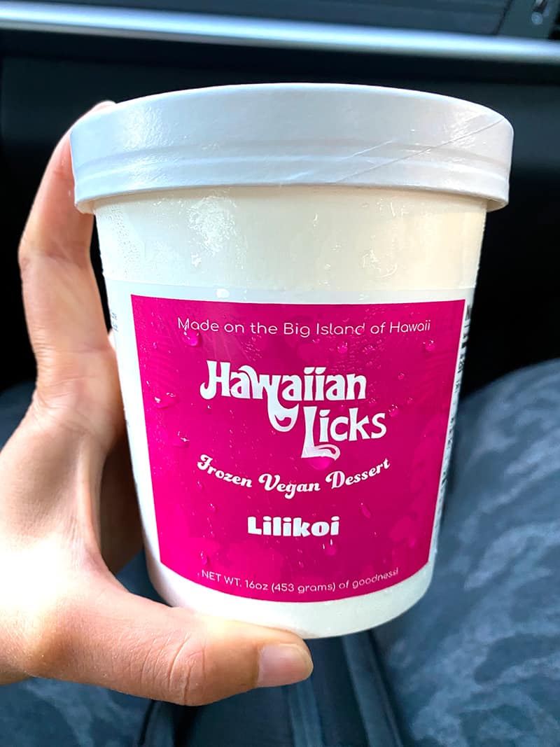 A hand is holding a carton of Hawaiian Licks lilikoi flavor vegan ice cream from the Big Island of Hawaii