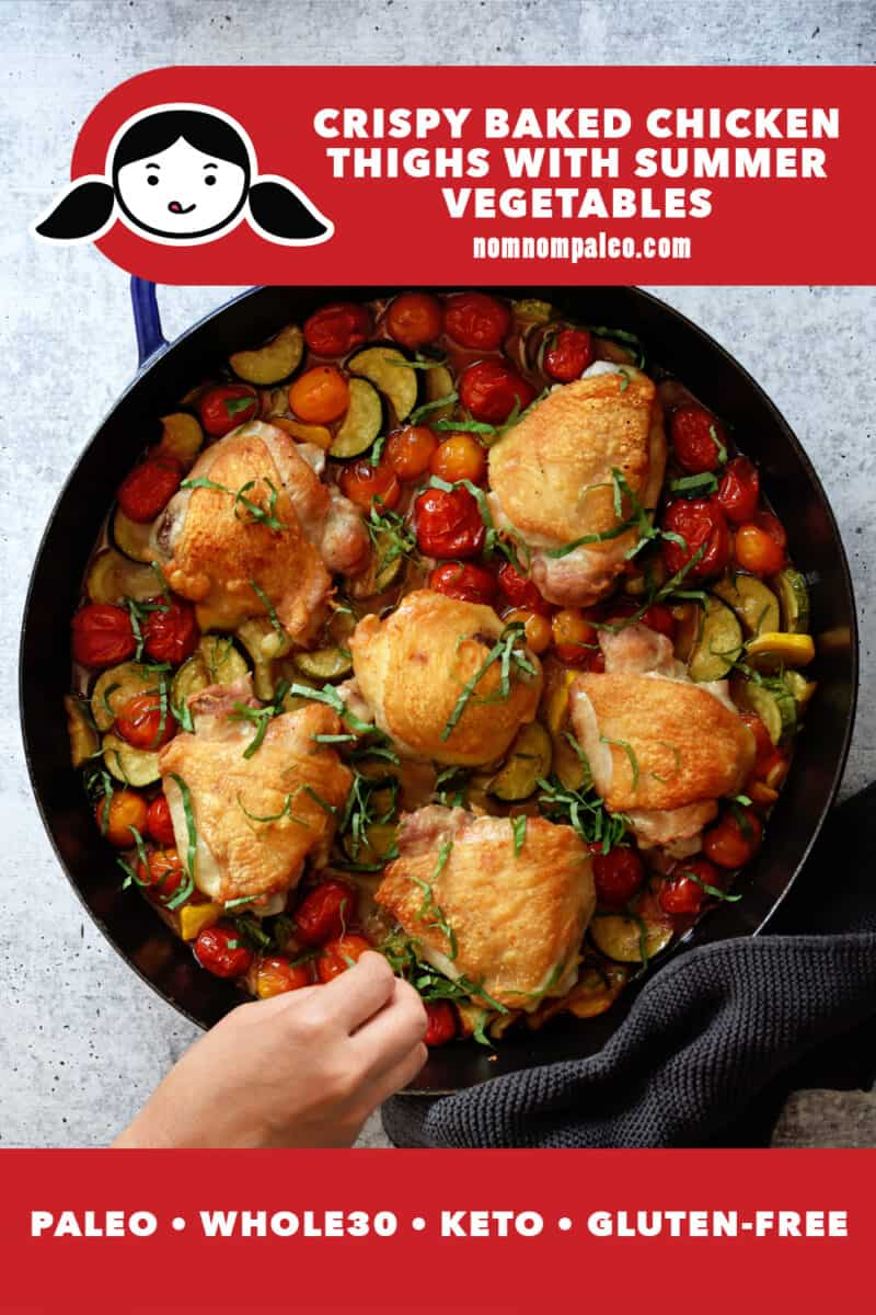An overhead shot of a large skillet filled with crispy oven baked chicken thighs and cherry tomatoes, zucchini, and basil.