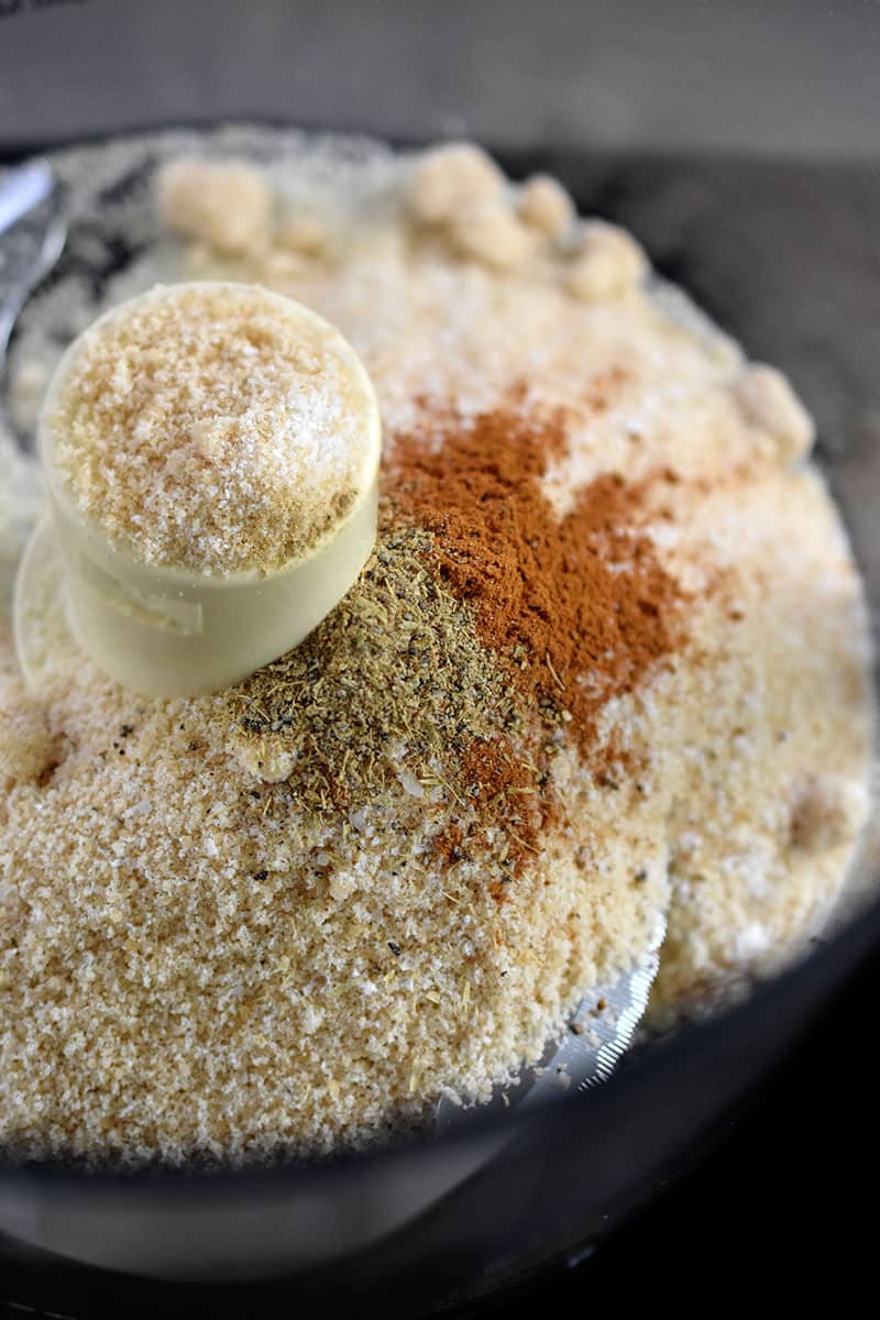 An overhead shot of an open food processor filled with almond flour, maple sugar, salt, cinnamon, and cardamom.