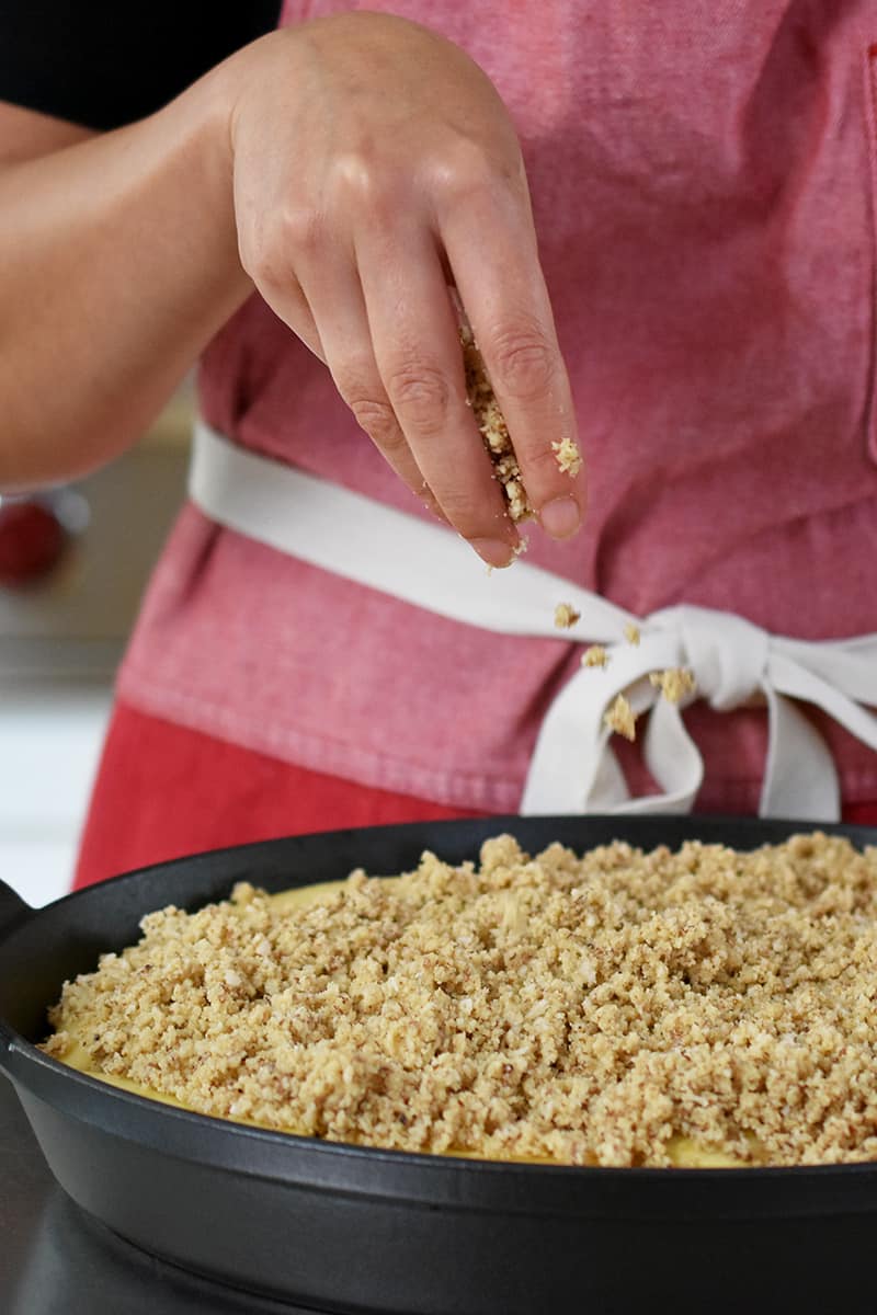 A hand is adding gluten-free, paleo topping onto an apple crisp.