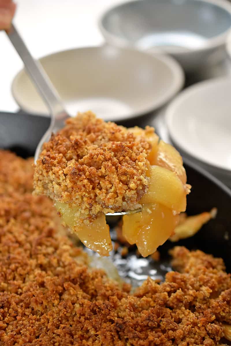 A spoon is scooping up paleo, vegan, and gluten-free apple crisp from a baking dish.
