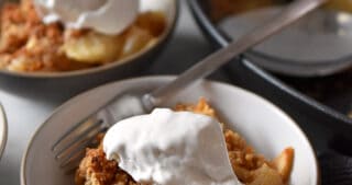 Two small dishes filled with paleo and gluten-free apple crisp and whipped coconut cream.