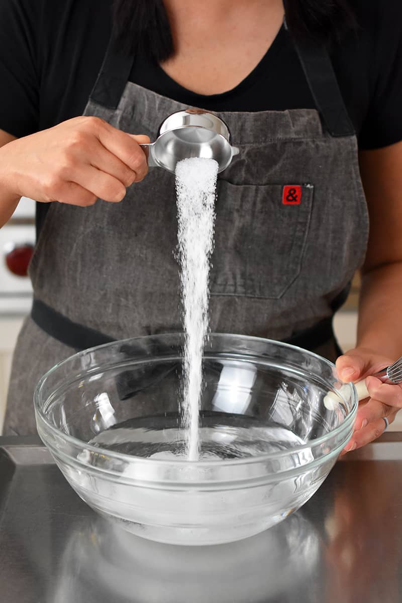 Someone in a gray apron is pouring salt into a bowl filled with water