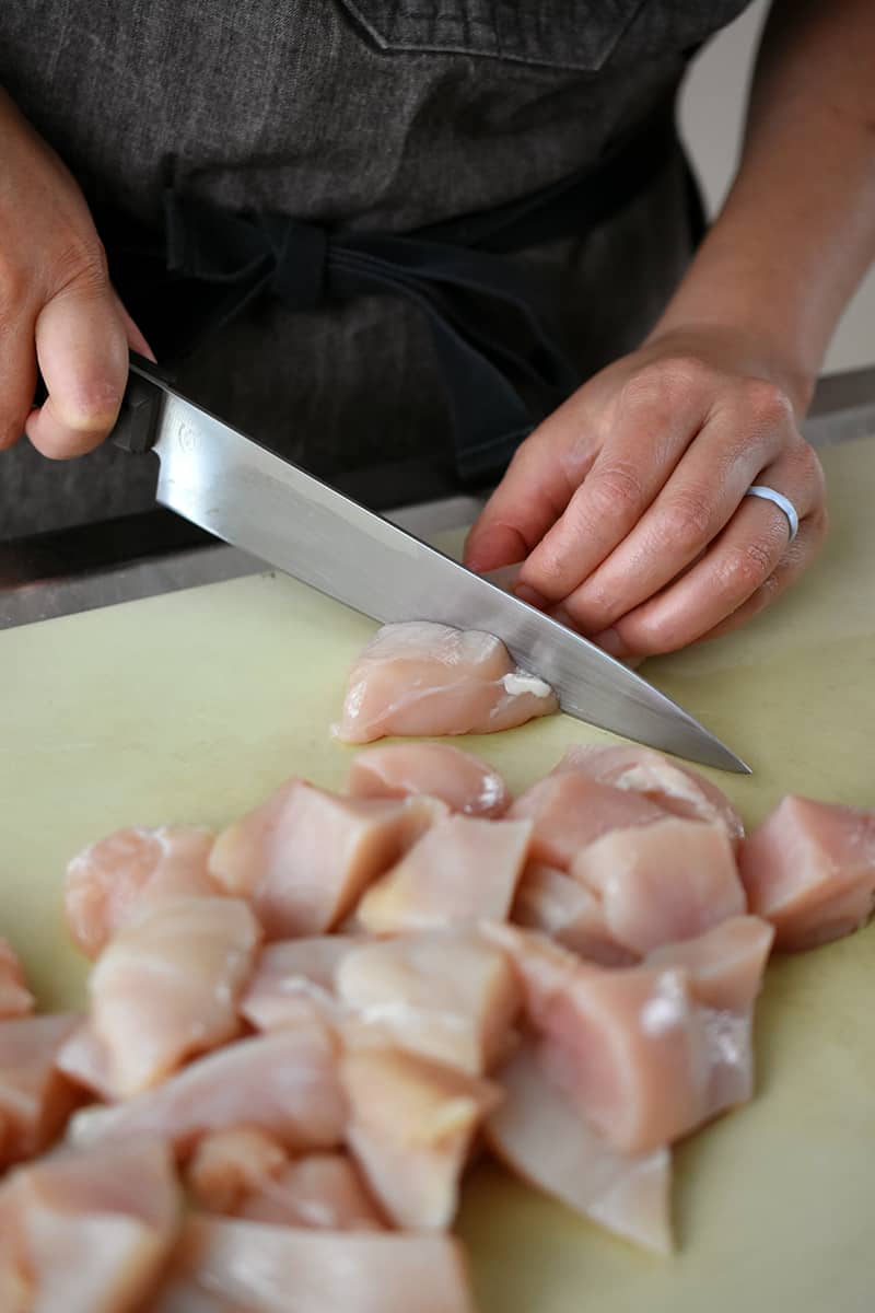 Cutting chicken breasts into bite-sized pieces on a cutting board.