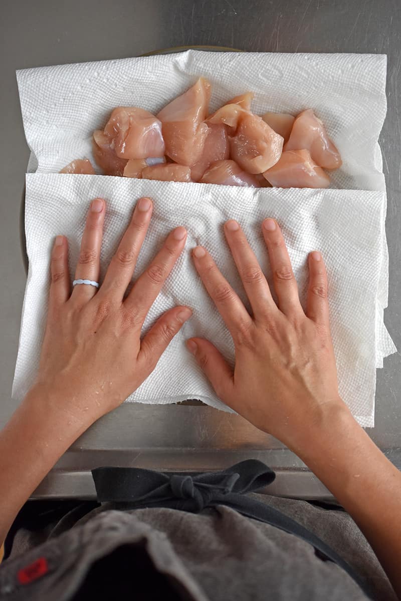 An overhead shot of someone patting brined chicken pieces with a paper towel on a plate.