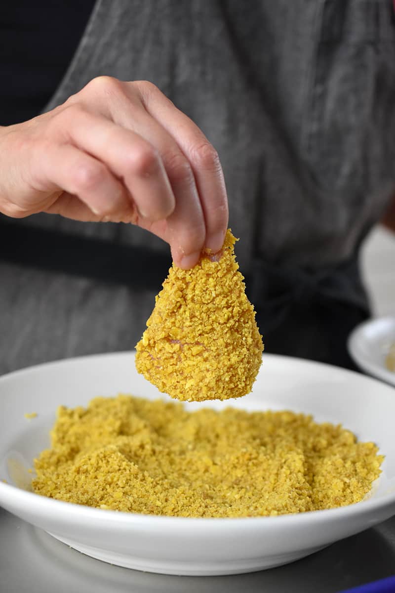 A hand removing a chicken nugget that has plantain crumbs on top.