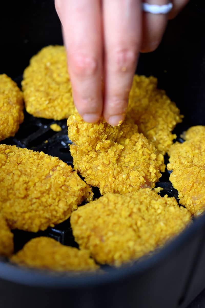 An overhead shot of a hand arranging chicken nuggets in a single layer in an air fryer basket.