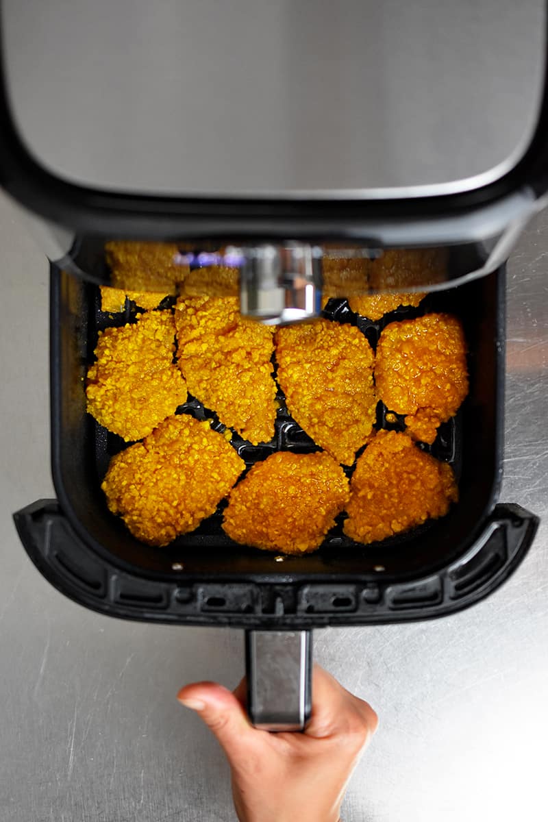 An overhead shot of an open air fryer with crispy paleo and gluten-free chicken nuggets inside.