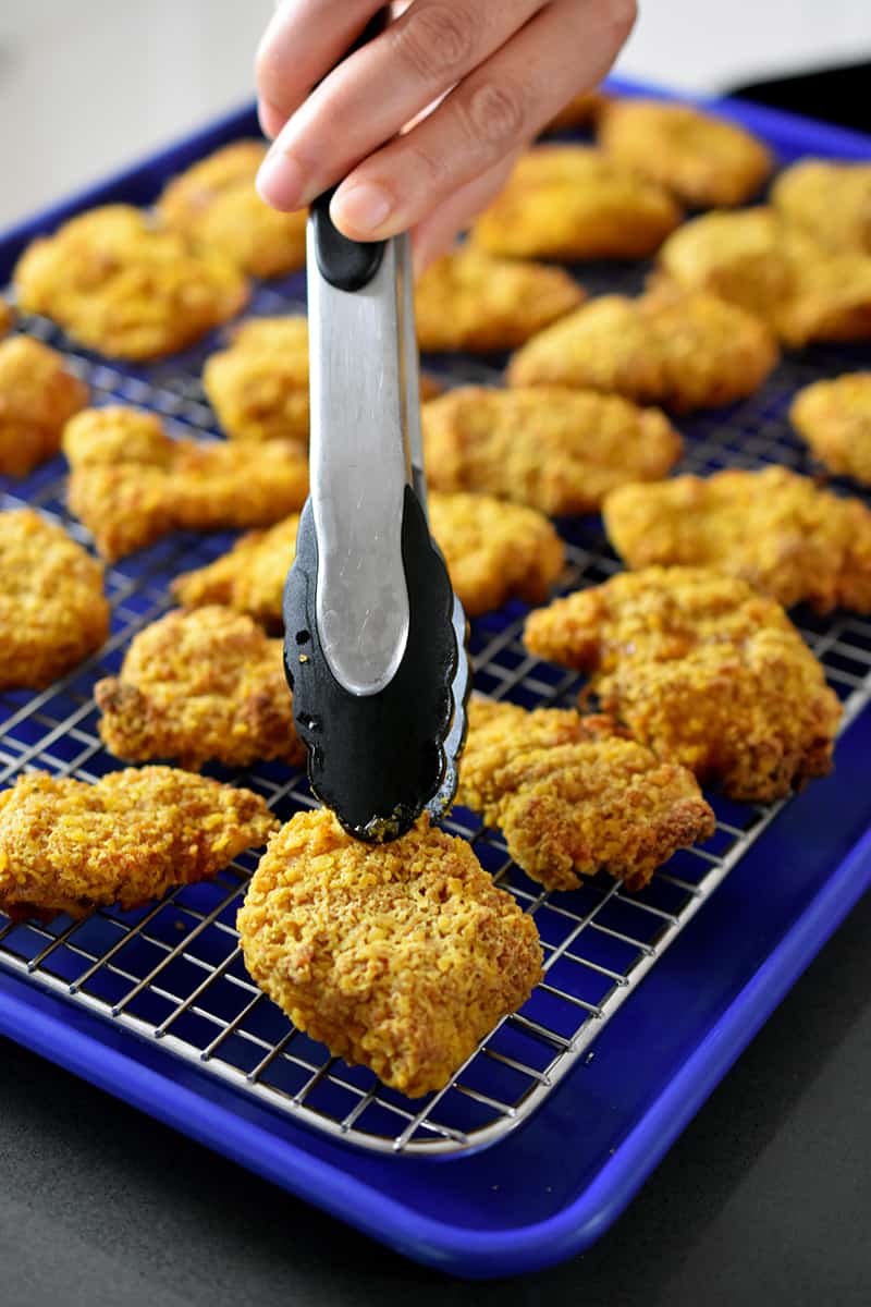 A pair of tongs are putting air fryer chicken nuggets on a rack 